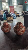 Pair of small ginger jars with orange floral patterns and rounded lids displayed on a dark wooden surface.