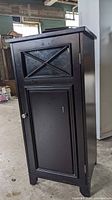 Front view of black wooden cupboard with door closed showing raised panel door with knob and solid wood construction.