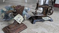 Photo of a vintage child's hand crank sewing machine, rusty metal picture stand, and a bag of assorted miniatures including plastic soldiers and dog tags