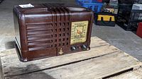 Side-front angled view of brown Emerson radio on wooden pallet showing tuning knob, power cord, and emblem.