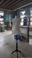 Full view of cream dress form mannequin standing in large room with industrial style windows and ceiling beams.