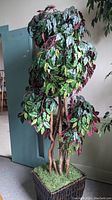 Full view of tall artificial tree with green and red leaves in a dark woven basket.