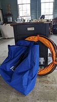 Photo showing folded orange agility tunnel rings alongside large blue nylon carrying case.