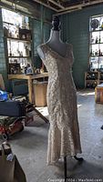 Full view of the beige lace dress on a mannequin in a rustic setting.