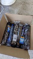 Open box containing multiple new fold-up umbrellas in original packaging with various printed covers including animal prints and plaid patterns.