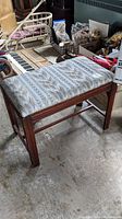 Wooden piano bench with patterned fabric upholstery and polished wood frame, showing overall structure and design.