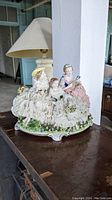 Porcelain figurine group of three ladies in detailed vintage-style dresses on a floral decorated base.