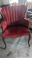 Front view of red upholstered armchair showing textured fabric, scalloped shell backrest, and curved wooden legs.