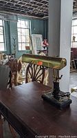 Photo showing vintage bankers style desk lamp with brass shade on heavy black marble base on wooden table