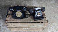 Two black vintage rotary dial telephones placed on a wooden crate, showing rotary dials and handsets