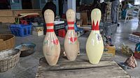 Three wooden bowling pins placed on a wooden surface, showing the front side with red striping and crown designs.