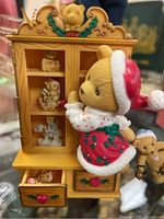 A detailed view of one Cherished Teddies figurine dressed in holiday costume climbing a miniature wooden cabinet with small teddy figures inside.