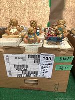 Photo showing collection of Cherished Teddies figurines displayed on top of their original boxes in a cardboard box.