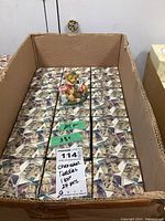 Box containing 24 individual Cherished Teddies figurine boxes with bear illustrations on the packaging and a sample figurine placed on top for display.