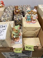 Lot of Cherished Teddies figurines displayed in original boxes inside a large cardboard box. Several figurines are visible on top of the boxes showing bears in detailed clothing.