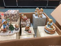 Lot of approximately 17 numbered Cherished Teddies porcelain figurines including bear with Christmas tree and animals, bear family group, and other scenes, shown in assortment on boxes.