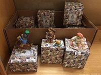 Wide photo showing multiple Cherished Teddies figures on top of their respective boxes inside a cardboard box. Some boxes are still unopened.