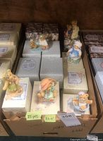 Photo showing 25 boxed Cherished Teddies figurines including several teddy bears in pastel outfits and different styles on top of original boxes inside a cardboard box