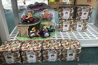 Display of five Cherished Teddies "Teddies In Motion" figurines on a stand with packaging boxes behind.