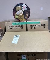 Set of cardboard boxes labeled with item number containing the tins, one tin displayed on top showing the bear and ornament inside.