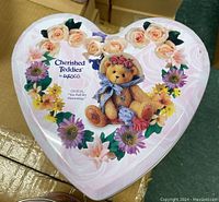 Heart-shaped tin top with teddy bear and floral design, brand and series info