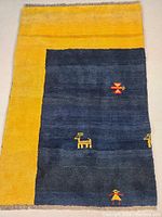 Full view of the rectangular Persian Gabbeh rug showing yellow border with dark blue central area and colorful small motifs including animals and human figure.