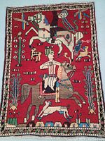 Full view of the Persian wool rug showing detailed horsemen and animal figures design on a red background.