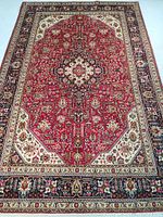 Full top-down view of hand knotted wool rug with red central field, ivory medallion, navy blue borders
