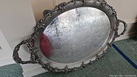 Full view of the antique silver plate platter featuring oval shape, two handles, an embossed floral and grapevine detailed outer rim and footed base.