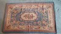 Full view of rectangular needlepoint area rug with central floral medallion and ornate scroll border in blue, cream, pink, and beige colors.