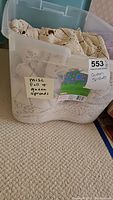 Plastic storage bin containing folded queen crocheted bedspreads, labeled as misc full & queen spreads.