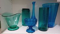 Five assorted blue and green glass items displayed on shelf.