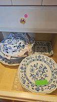 Photo of several blue and white transferware plates stacked in a drawer, including dinner plates and a covered serving dish.