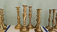 Six antique brass candlesticks displayed together showing different traditional shapes and heights.