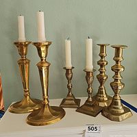 Full view of three pairs of solid brass candlesticks displayed on a white surface with white taper candles.