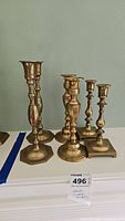 Group view of six brass candlesticks showing various shapes and heights.