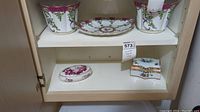 Two white ceramic planters with grapevine design and a decorative plate on a shelf