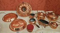 Full set of copper kitchenware displayed including decorative moulds, Bundt pan, kettles, gravy boat, serving pots, and cleaning product