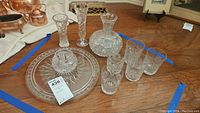 Full view of the crystal and glass set including vase, decanter, flute, glasses, and platter on wooden floor.