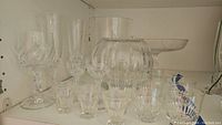 Shelf display of crystal and pressed glassware including bowls and glasses with cut patterns