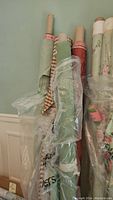 Several partial rolls of fabric including green, plaid, red paisley, and floral prints, seen rolled on cardboard tubes with some wrapped in plastic