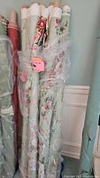 Rolls of decorator fabric with green floral polished chintz wrapped in plastic and with tags.