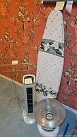 Photo showing the Atlantic Breeze tower fan, Presto Heat Dish heater, and ironing board with floral cover against a floral wallpaper background.