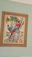 Full view of the framed textile artwork showing two vibrantly colored birds perched on a rock with floral background.