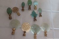 Overview of 11 lamp finials on a white surface showing jade and ivory pieces with metal bases