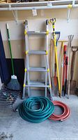 Photo showing Little Giant aluminum multi-position ladder, garden hoses, broom, and various yard tools.