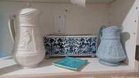 Two antique pitchers, an Asian style flower brick, and a small turquoise ceramic dish on a white shelf.