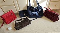 Five purses arranged on carpet near dressers, showing color, style, and general condition