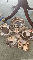 Overview of all seven silverplated serving items displayed on floor under table, showing bowls, platters, teardrop dishes and covered container.