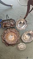 Overview of 5 silverplated items on carpet showing shape and ornate embossed decoration